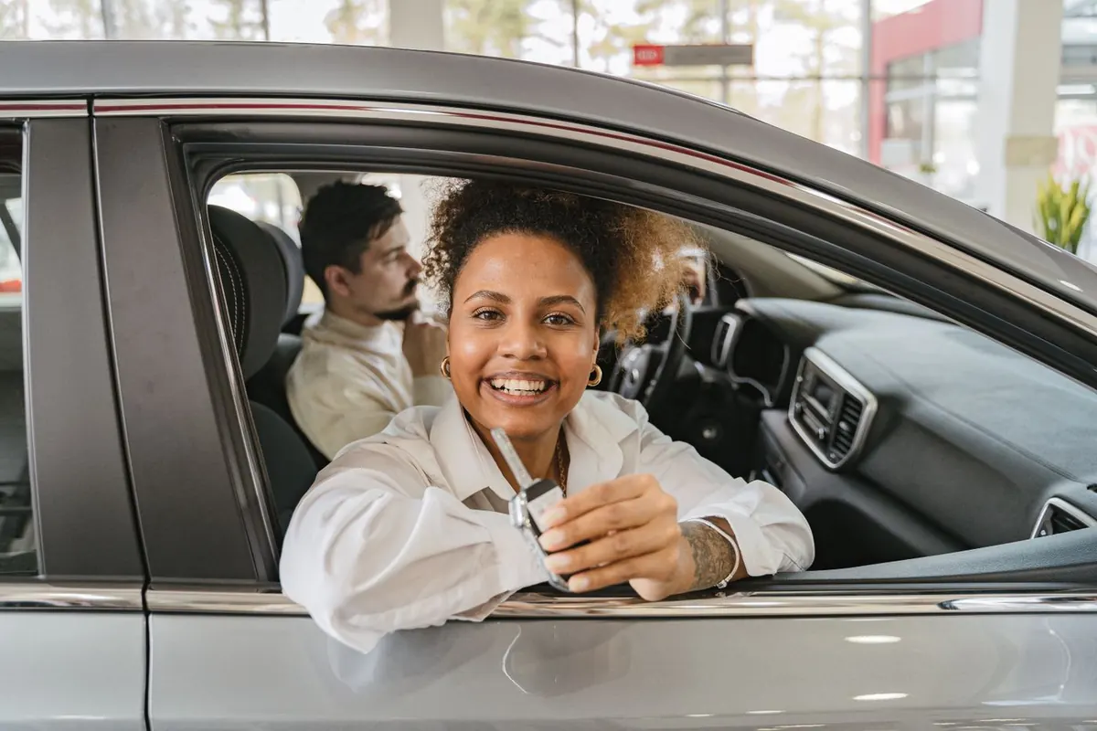 Eine Frau am Steuer eines neuen Autos hält den Autoschlüssel bei einem Autohändler