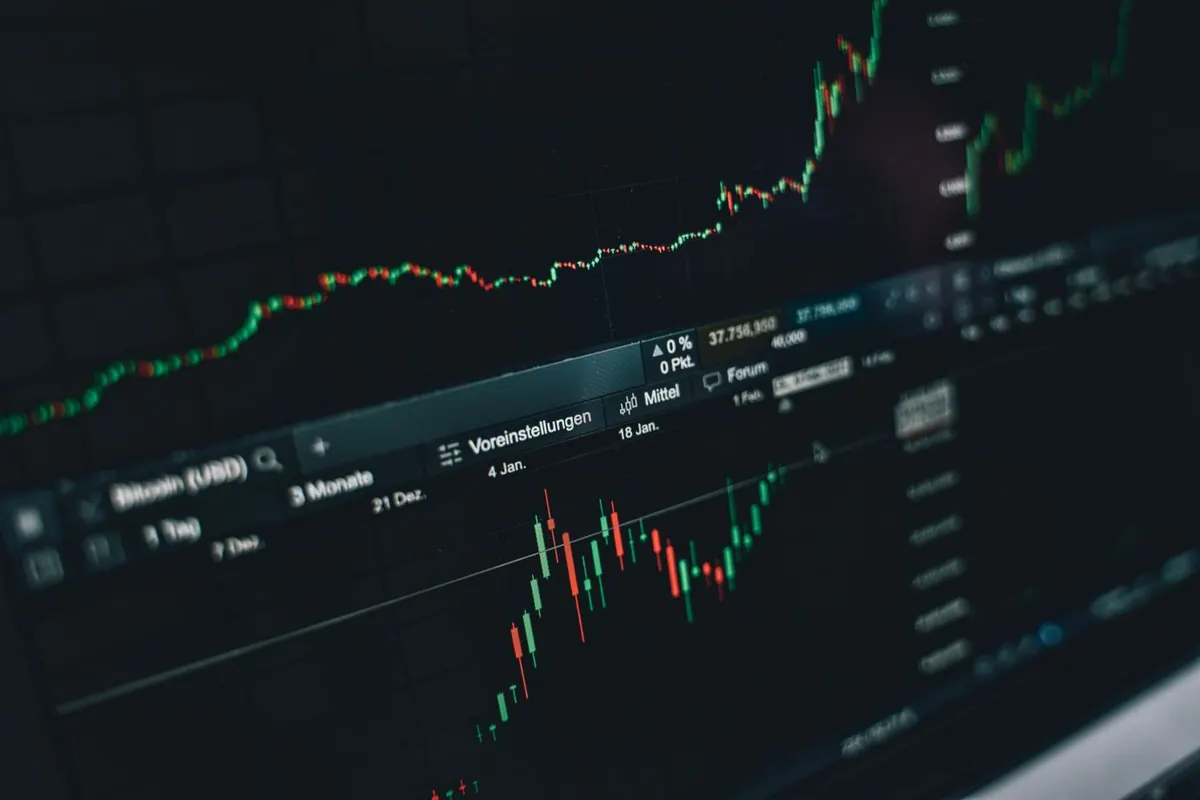 Stock market charts on a screen next to a phone with an investing app, comparing US brokerage accounts