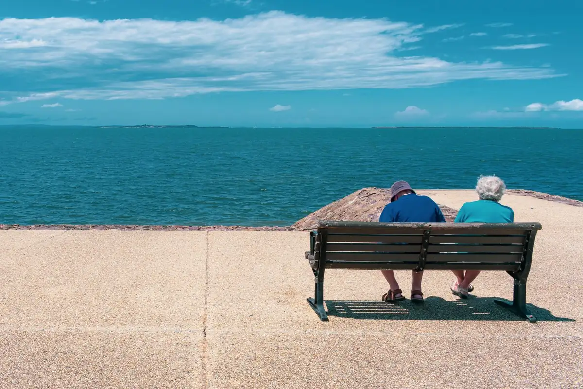 An older couple sitting on a bench looking out at the sea, representing a comfortable retirement