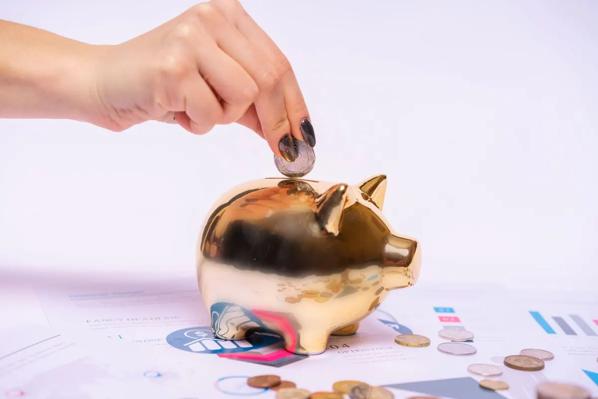 Persona metiendo una moneda en una hucha, ilustrando cómo ahorrar más dinero cada mes