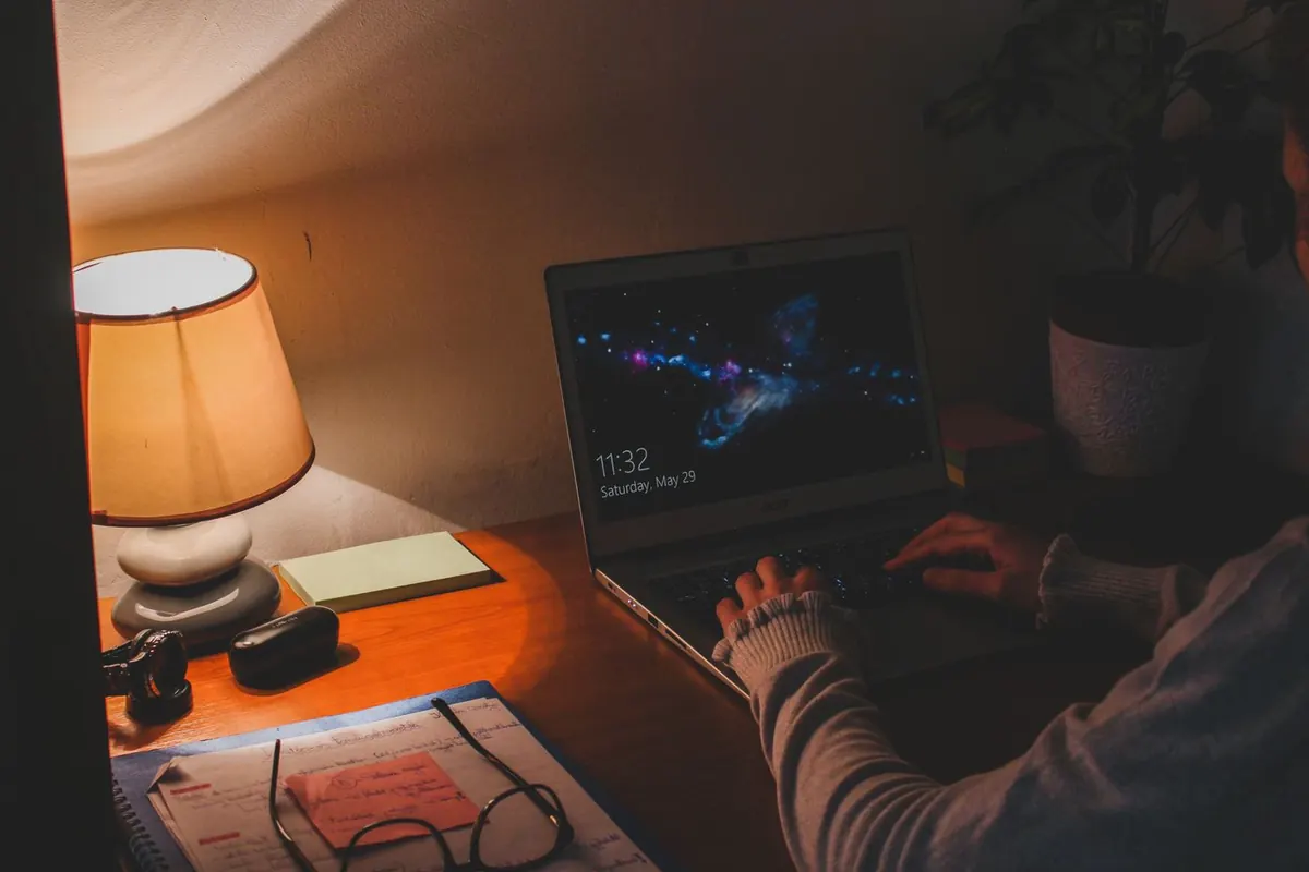 Persona trabajando en un portátil en casa por la noche, buscando cómo ganar más dinero