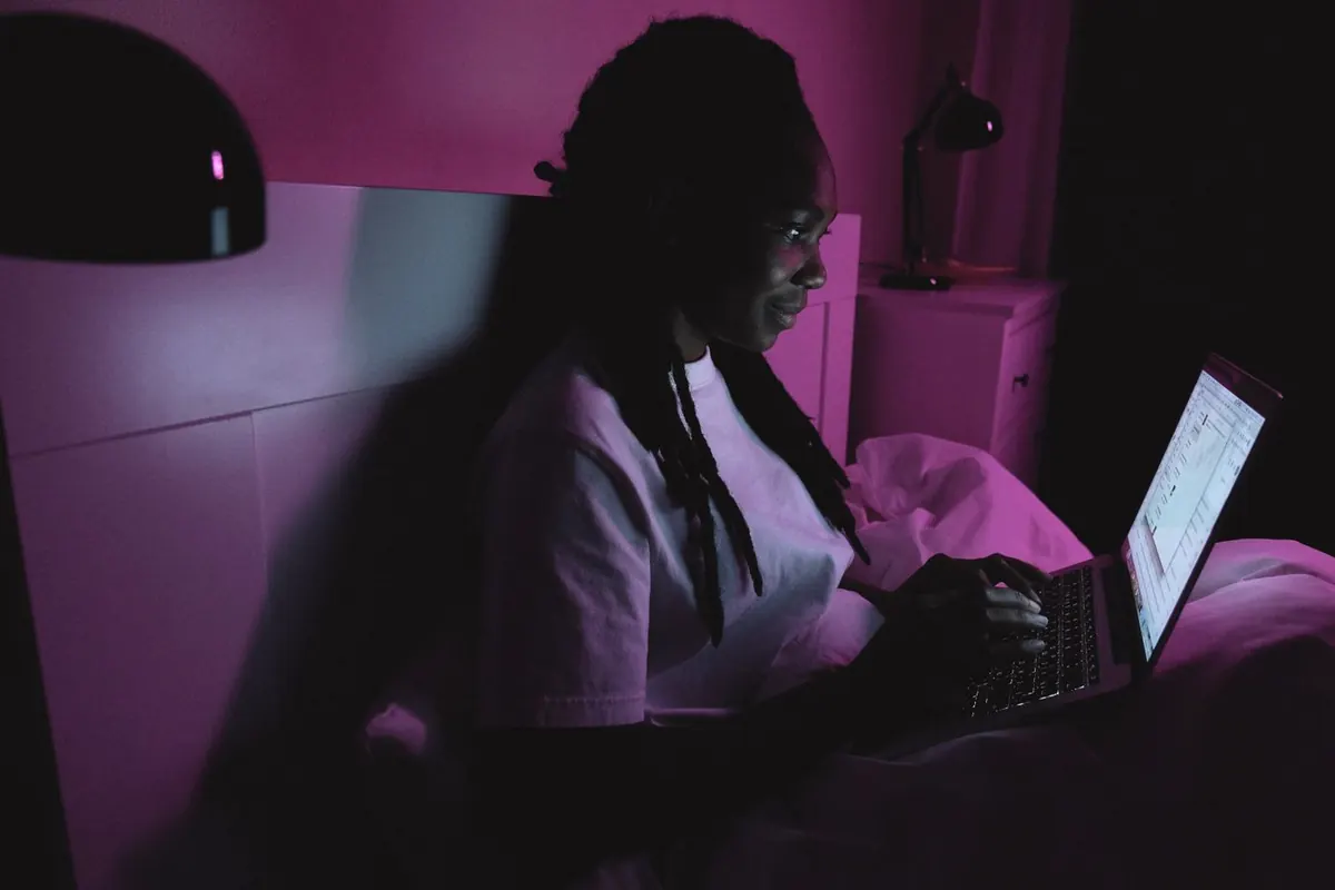 A person working on a laptop at home in the evening, figuring out how to make more money