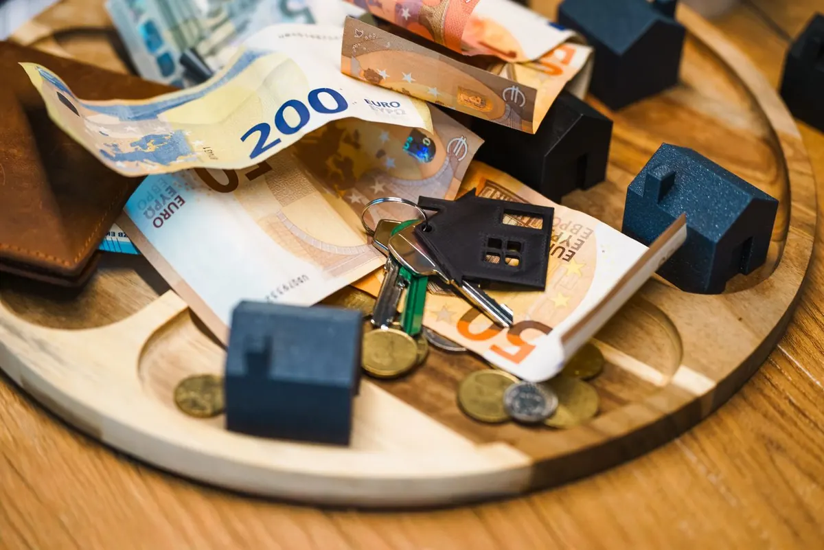 Billetes de euro, monedas, casas en miniatura y llaves sobre una bandeja, símbolo de una herencia y su fiscalidad