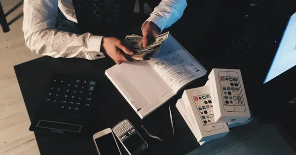 Person counting banknotes at a desk next to a calculator and a notebook