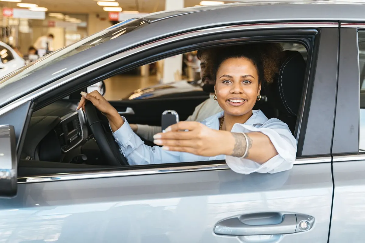 Une femme au volant d'une voiture neuve tenant la clé chez un concessionnaire