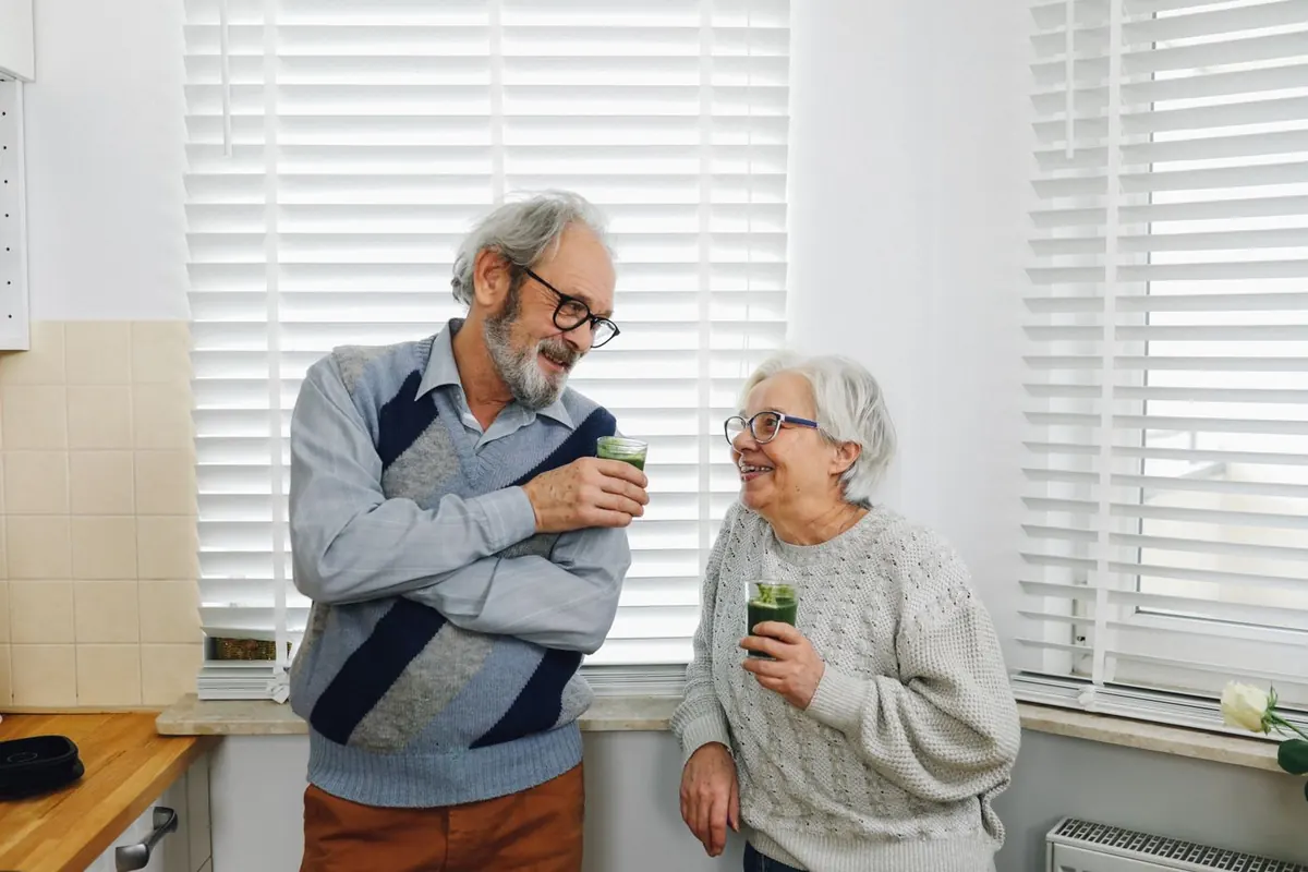 Couple de personnes âgées discutant dans leur cuisine, un verre à la main, illustrant une retraite sereine