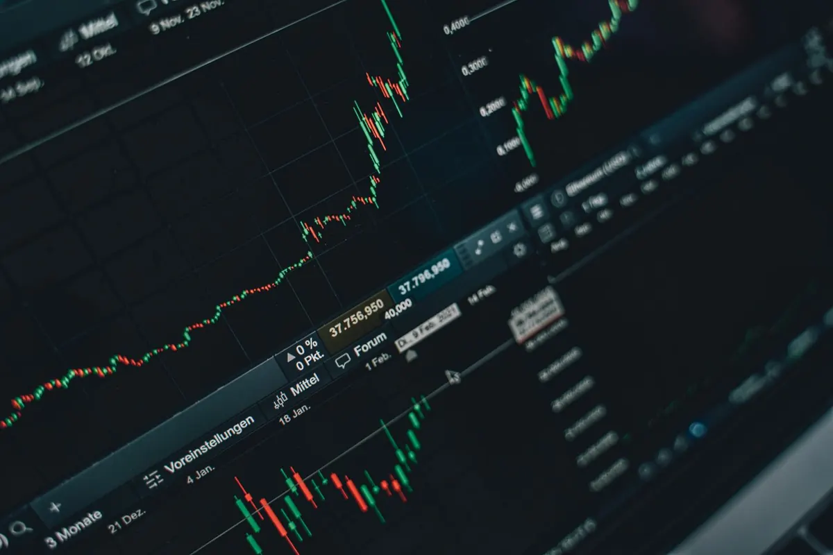 Pantalla con gráficos de bolsa y un teléfono con una app de inversión, comparativa de brokers en España