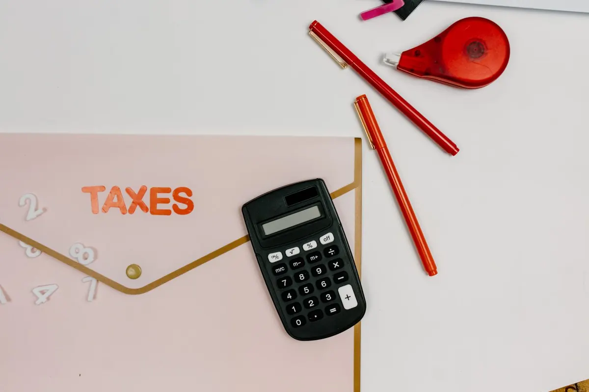 Flatlay mit einer Mappe mit der Aufschrift Taxes, einem Taschenrechner und roten Stiften