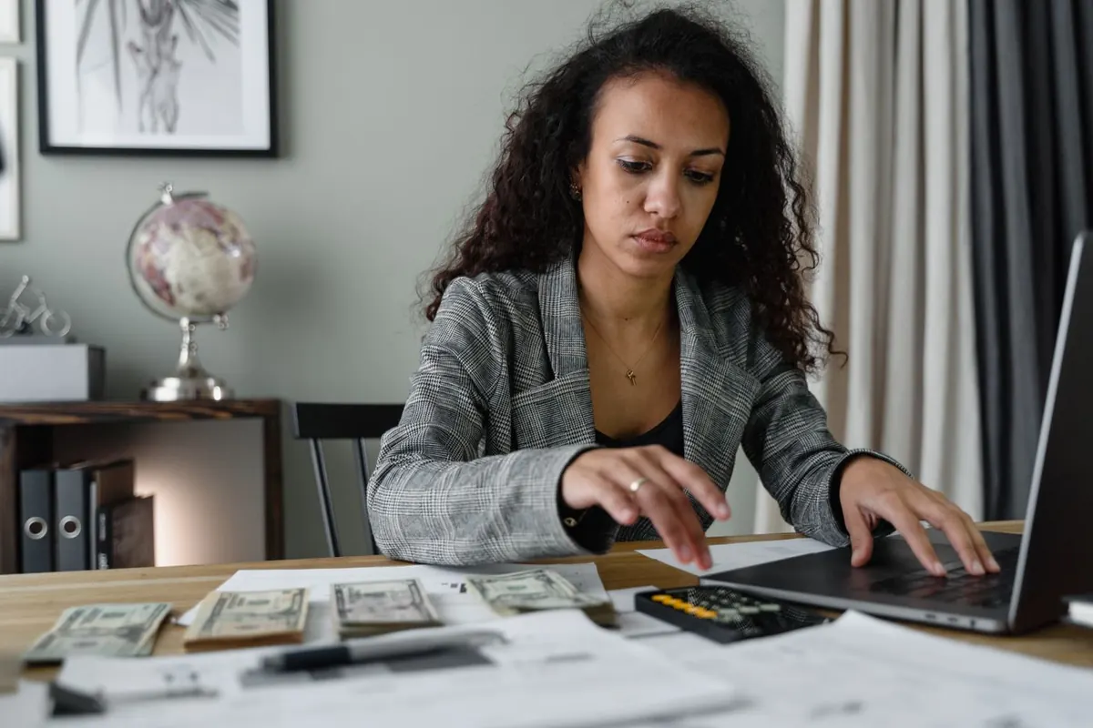Femme assise à un bureau avec des billets, une calculatrice et un ordinateur portable