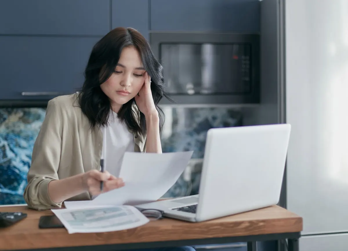 A freelancer reviewing paperwork at a laptop while managing her taxes